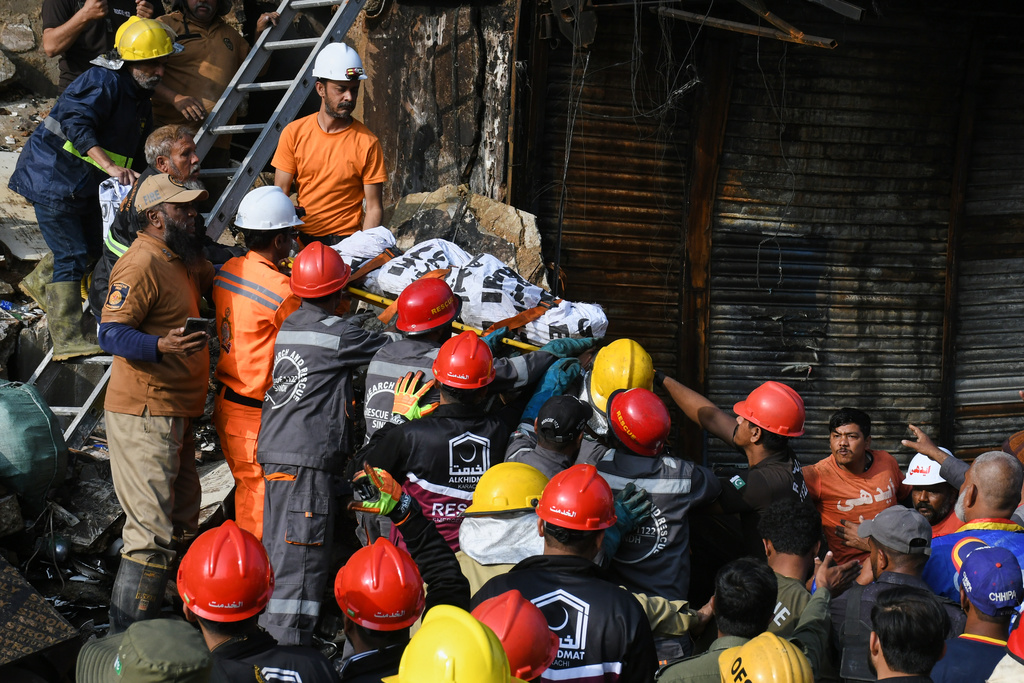 Firefighters transport a body after recovering from the rubble of a burnt building of a multi-story shopping plaza following a massive fire in Karachi, Pakistan, Monday, Jan. 19, 2026. (AP Photo/Ali Raza)
