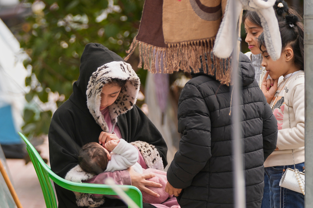 A displaced girl feeds a baby as other children stand at tents sheltering people who fled Israeli airstrikes in Dahiyeh, in Beirut's southern suburbs, along the wall of the Pine Residence, the official residence of the French ambassador, in Lebanon. (AP Photo/Hassan Ammar)