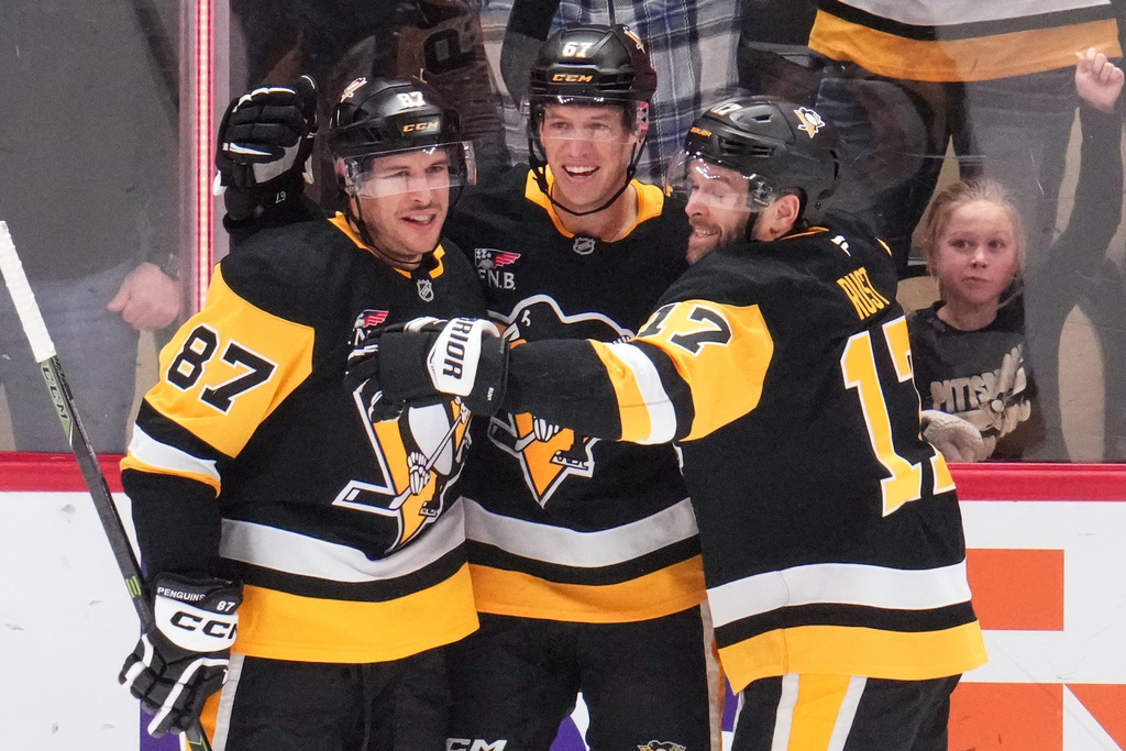 Pittsburgh Penguins' Sidney Crosby (87) celebrates with Rickard Rakell and Bryan Rust (17) after taking over from former Penguins player Mario Lemieux as the team's all-time points leader during the first period of an NHL hockey game against the Montréal Canadiens in Pittsburgh, Sunday, Dec. 21, 2025. (AP Photo/Gene J. Puskar)