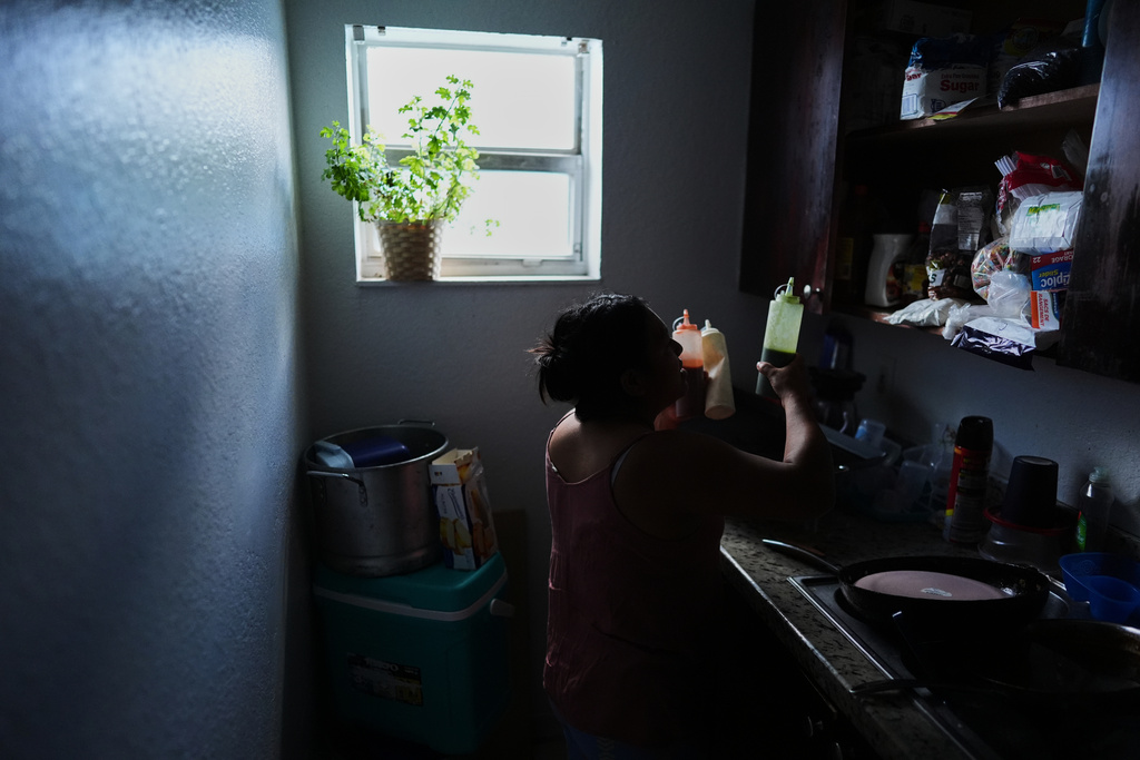 Guatemalan migrant Amavilia, 31, gets out the sauces she uses to flavor the corn on the cob she sells, inside her South Florida apartment, Wednesday, Oct. 8, 2025, after her infant son's father, who worked in construction, was detained and deported to Guatemala. (AP Photo/Rebecca Blackwell)