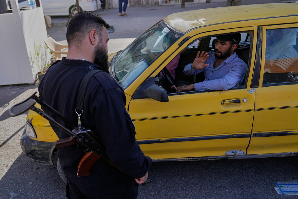 A taxi driver waves to a Syrian government security man at a checkpoint, in the southern Damascus suburb of Jaramana, Syria, Friday, Oct. 3, 2025. (AP Photo/Hussein Malla)