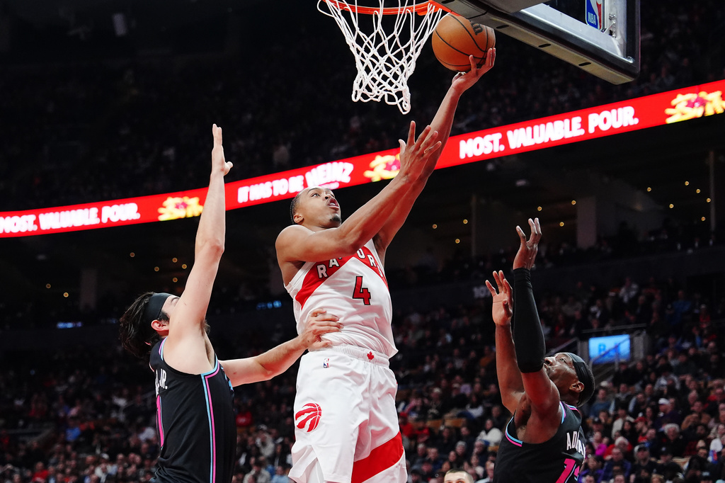 Toronto Raptors' Scottie Barnes (4) scores between Miami Heat's Jaime Jaquez Jr., left, and Bam Adebayo, right, during the first half of an NBA basketball game in Toronto on Tuesday, April 7, 2026. (Frank Gunn/The Canadian Press via AP)