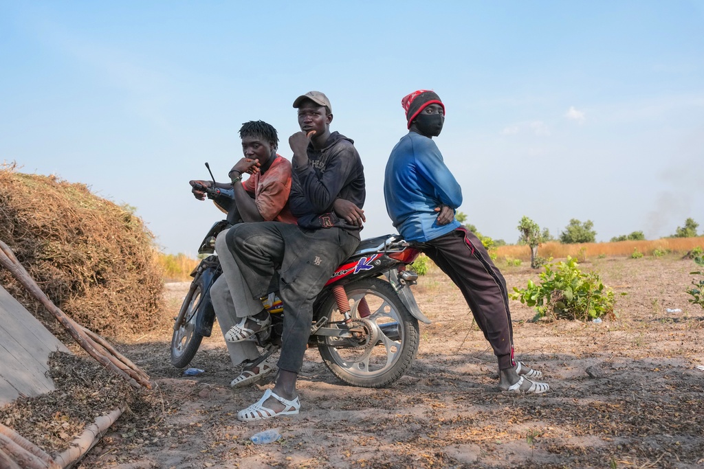 Issa Traore, left, Mamadou Camara, center, and Madassa Kebe, who moved from Mali to Senegal to pursue farming, sit on a scooter on a farm in Tambacounda, Senegal, Wednesday, Nov. 5, 2025. (AP Photo/Mark Banchereau)