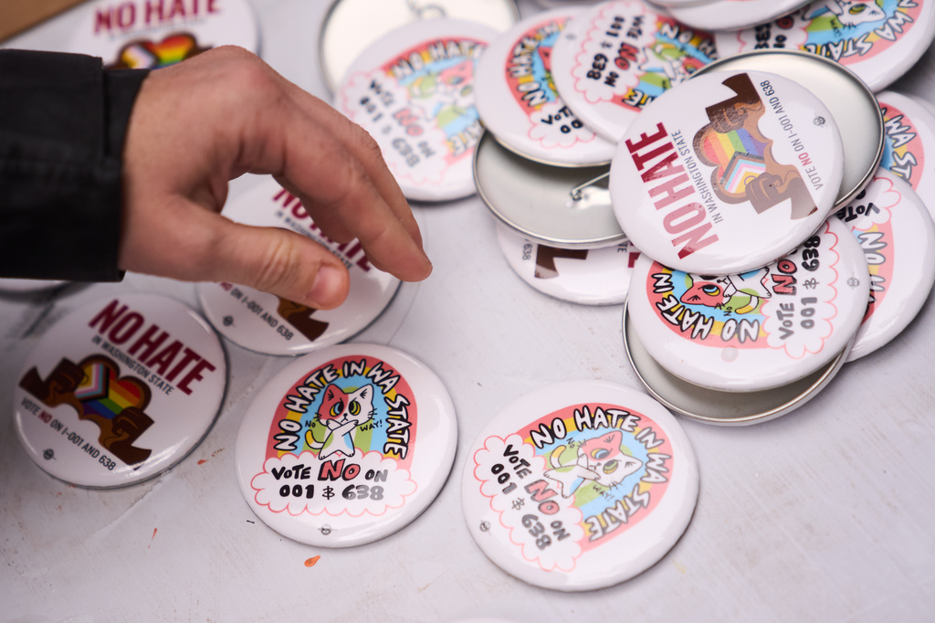 A person picks up a button during a "No Hate in WA State" rally against multiple initiatives on the November ballot, including Washington State Initiative 638, which would prohibit transgender girls from competing in girls' sports, Saturday, Oct. 17, 2026, in Seattle. (AP Photo/Lindsey Wasson)