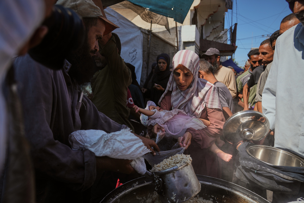 Palestinians receive donated food at a community kitchen in Deir al-Balah, central Gaza Strip, Thursday, Oct. 16, 2025. (AP Photo/Abdel Kareem Hana)