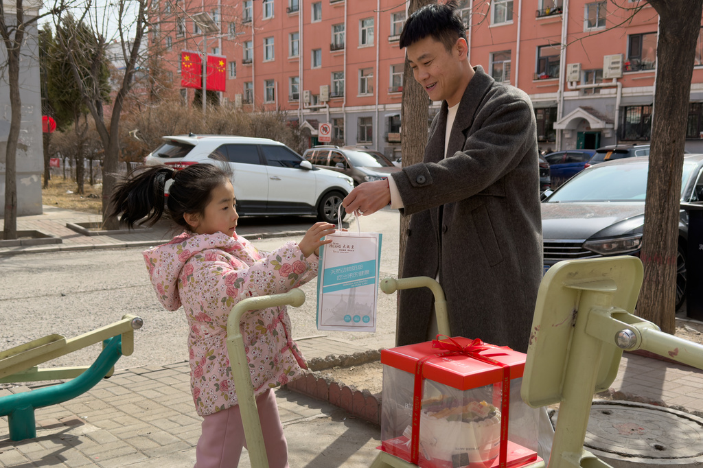 Zhou Hongfei, a coal miner, holds a bag out to his daughter at a residential complex for former and current coal miners in Datong, China, Saturday, March 14, 2026. (AP Photo/Ng Han Guan)