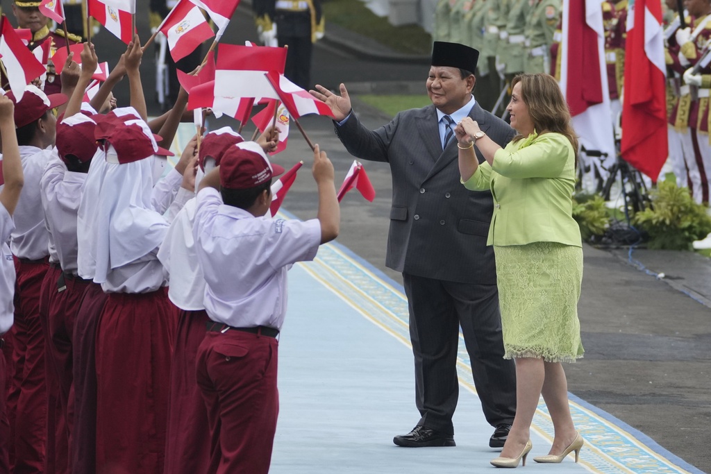 Peruvian President Dina Boluarte, right, and Indonesian counterpart Prabowo Subianto greet children waving Indonesian and Peruvian flags during a welcoming ceremony prior to their meeting at Merdeka Palace in Jakarta, Indonesia, Monday, Aug. 11, 2025. (AP Photo/Achmad Ibrahim)