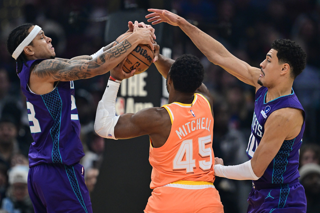Charlotte Hornets guard Tre Mann, left, and guard Josh Green, right, defend against Cleveland Cavaliers guard Donovan Mitchell in the first half of an NBA basketball game, Monday, Dec. 22, 2025, in Cleveland. (AP Photo/David Dermer)