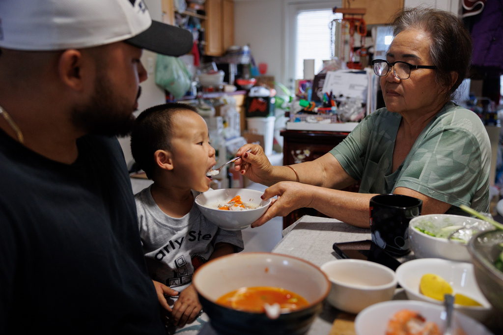 Lien Chang feeds her 2-year-old grandson Cairo Miu a bowl of rice next to his dad Jack Chang in her home on Monday, July 13, 2026, in San Francisco. (AP Photo/Juliana Yamada)