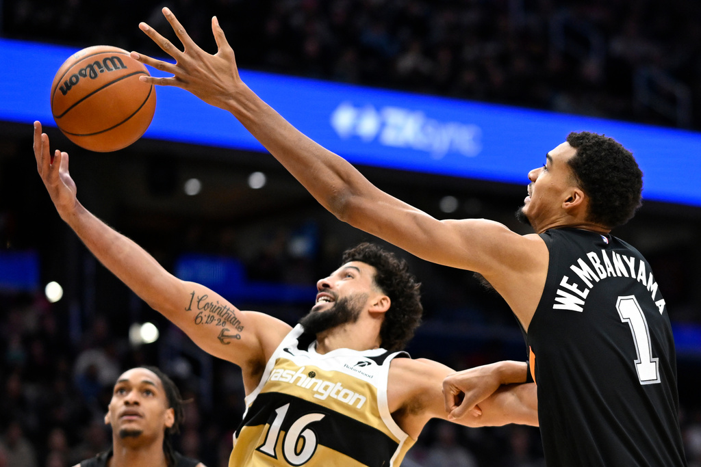 Washington Wizards forward Anthony Gill (16) grabs a round against San Antonio Spurs forward Victor Wembanyama (1) during the first half of an NBA basketball game, Sunday, Dec. 21, 2025, in Washington. (AP Photo/John McDonnell)