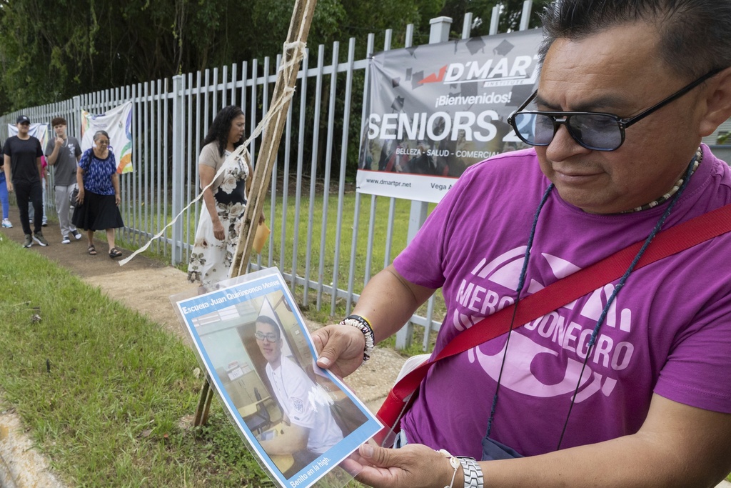 A visitor on a guided tour holds a photo of Bad Bunny outside Juan Quirindongo Morell High School, where the music star completed his secondary studies, in Vega Baja, Puerto Rico, Tuesday, Aug. 12, 2025. (AP Photo/Alejandro Granadillo)