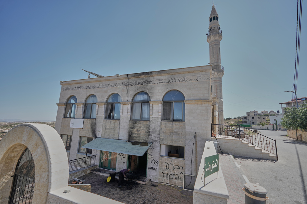 A man clears the rubble as writing in Hebrew on the wall reads "revenge, regards to the arrested, people, wake up," at one of the West Bank mosques that were vandalized and partly set on fire by Israeli settlers overnight, in the village of Jiljilya, north of Ramallah, Wednesday, June 17, 2026. (AP Photo/Majdi Mohammed)