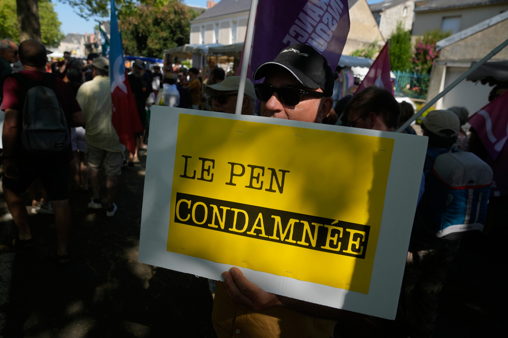 A protestor holds a placard reading: Le Pen convicted, during a protest against the visit of far-right leader Marine Le Pen in La Fleche, western France, Wednesday, July 8, 2026. (AP Photo/Michel Euler)
