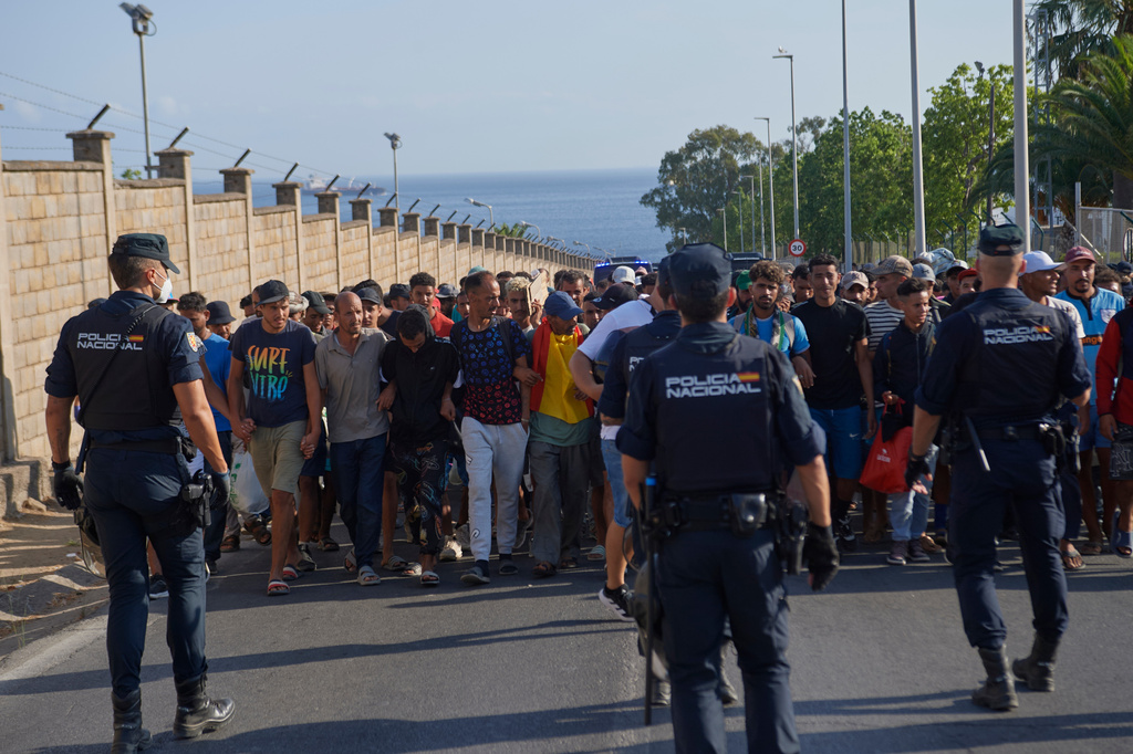 Migrants who crossed from Morocco into Spain are escorted by Spanish police to temporary shelters after being cleared from a beach in the Spanish exclave of Ceuta on Thursday, Aug. 20, 2026. (AP Photo/Antonio Sempere)