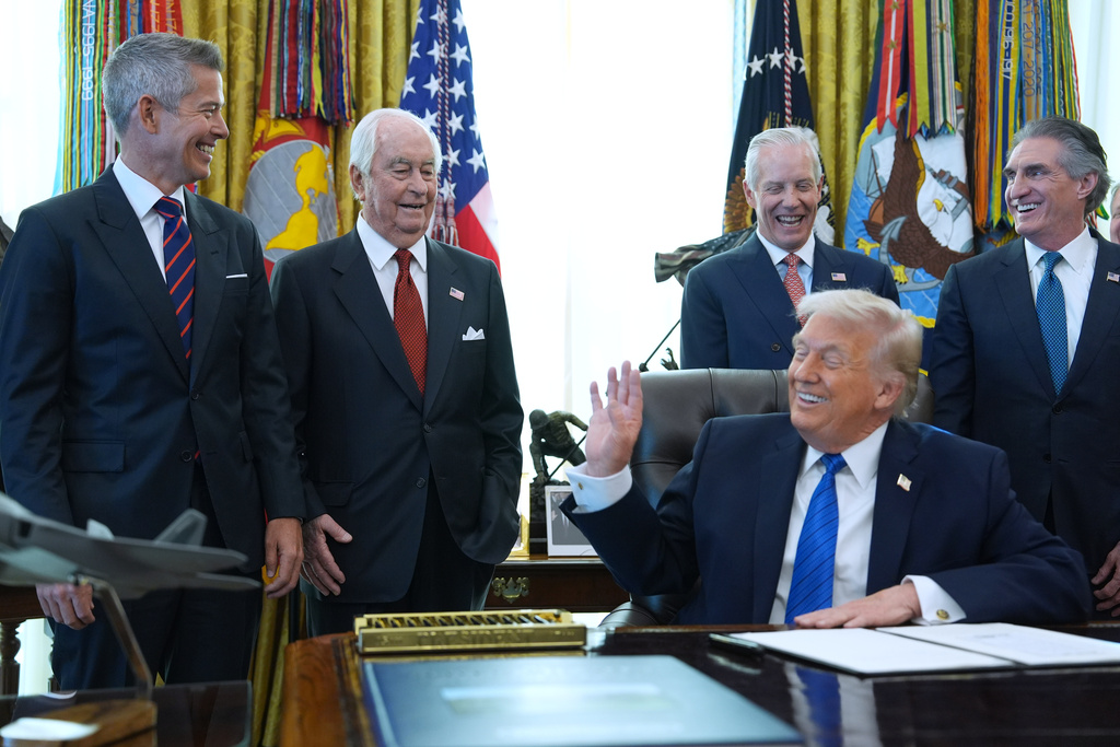 President Donald Trump speaks to Roger Penske, second left. as he signs executive orders in the Oval Office of the White House, Friday, Jan. 30, 2026, in Washington. (AP Photo/Evan Vucci)