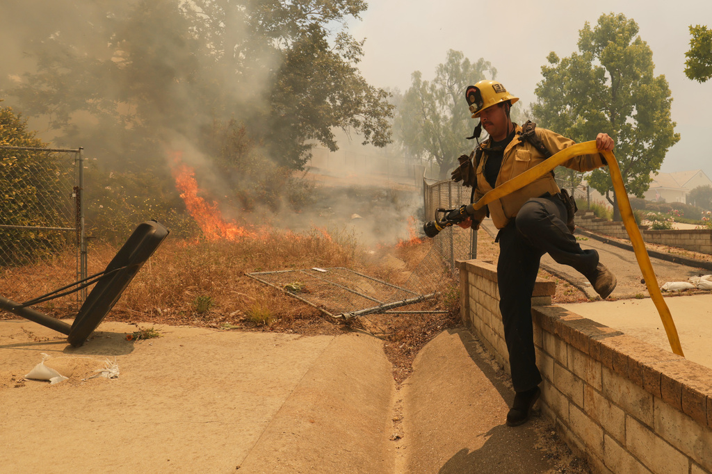 A firefighter hops over a fence while battling the Sandy Fire Monday, May 18, 2026, in Simi Valley, Calif. (AP Photo/Ethan Swope)