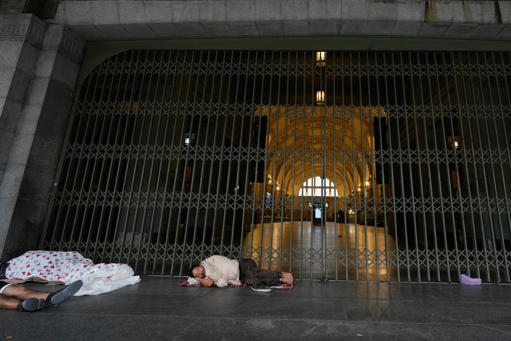 People sleep near the closed entrances of Constitucion railway station during a union strike against President Javier Milei’s proposed labor reform bill in Buenos Aires, Argentina, Thursday, Feb. 19, 2026. (AP Photo/Gustavo Garello)
