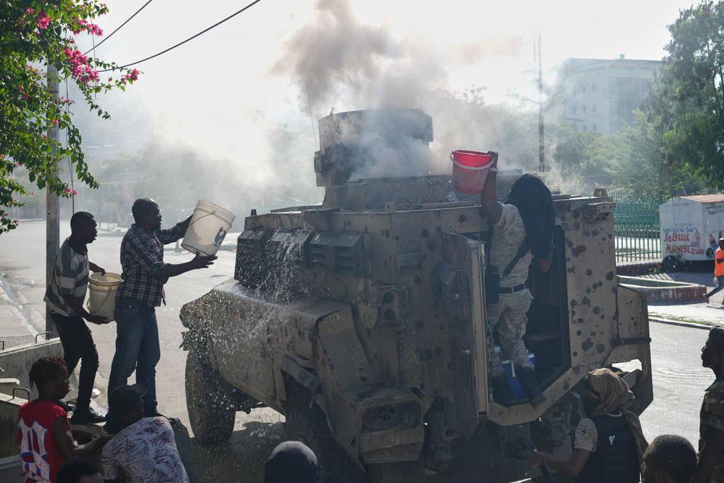 Police and civilians attempt to put out a fire set by gang members on an armored police vehicle in a gang-controlled area of Port-au-Prince, Haiti, Monday, Jan. 19, 2026. (AP Photo/Odelyn Joseph)