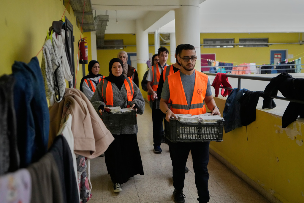 Volunteers carrying meals to be distributed for displaced people who fled Israeli strikes from south Lebanon at a school turned into a shelter, in the southern port city of Sidon, Lebanon, Saturday, March 14, 2026. (AP Photo/Mohammed Zaatari)