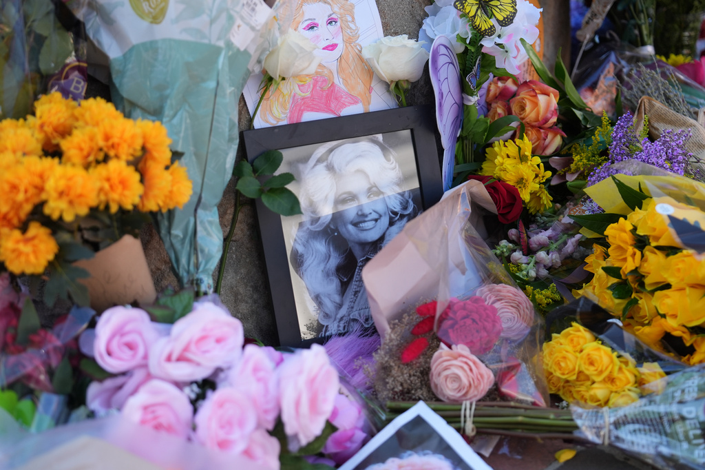 Images and flowers form a makeshift memorial honoring Dolly Parton in front of her statue in Sevierville, Tenn., Tuesday, Aug. 25, 2026. (AP Photo/Camden Hall)