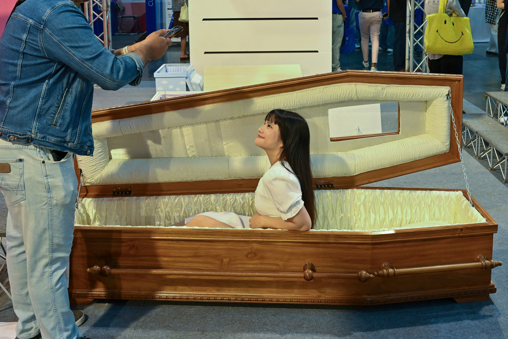 A visitor poses for a photo sitting in a coffin at Death Fest in Nonthaburi, Thailand, Friday, March 13, 2026. (AP Photo/Kittinun Rodsupan)