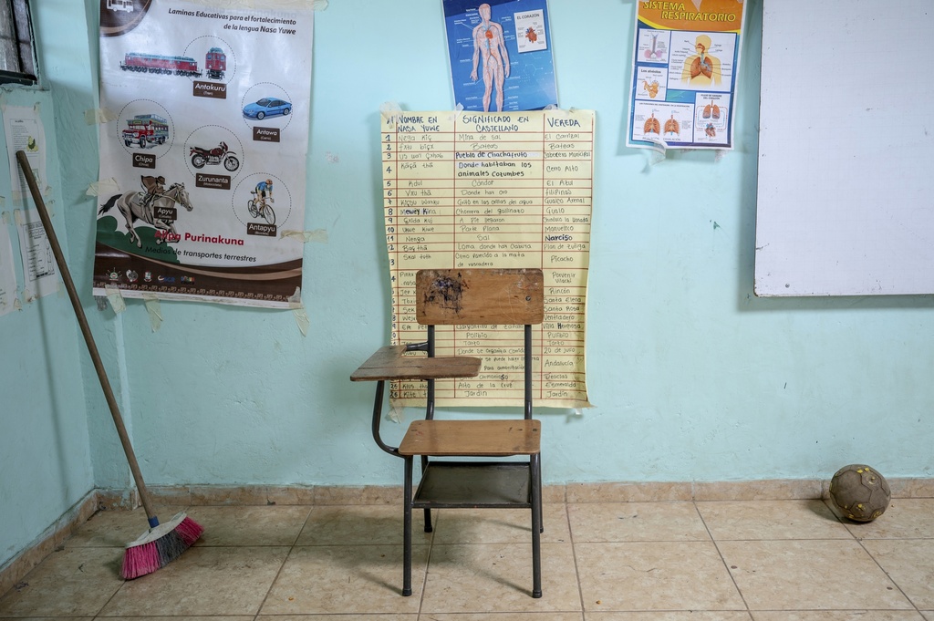 In a classroom at a school, a desk sits near posters displaying educational information, some in the Nasa Yuwe language, on July 18, 2025, in Manuelico village, Caldono, Colombia. (AP Photo/Nadège Mazars)