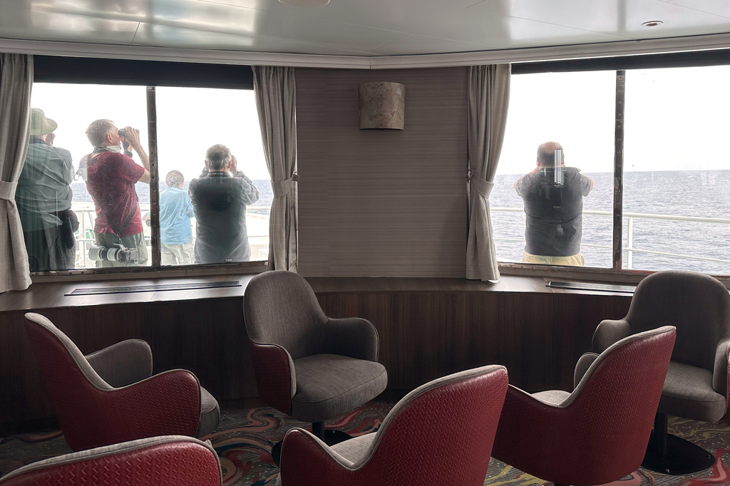Passengers on the hantavirus-stricken cruise ship, MV Hondius, scan the horizon with binoculars during their voyage to Spain's port of Tenerife, May 6, 2026. (AP Photo)