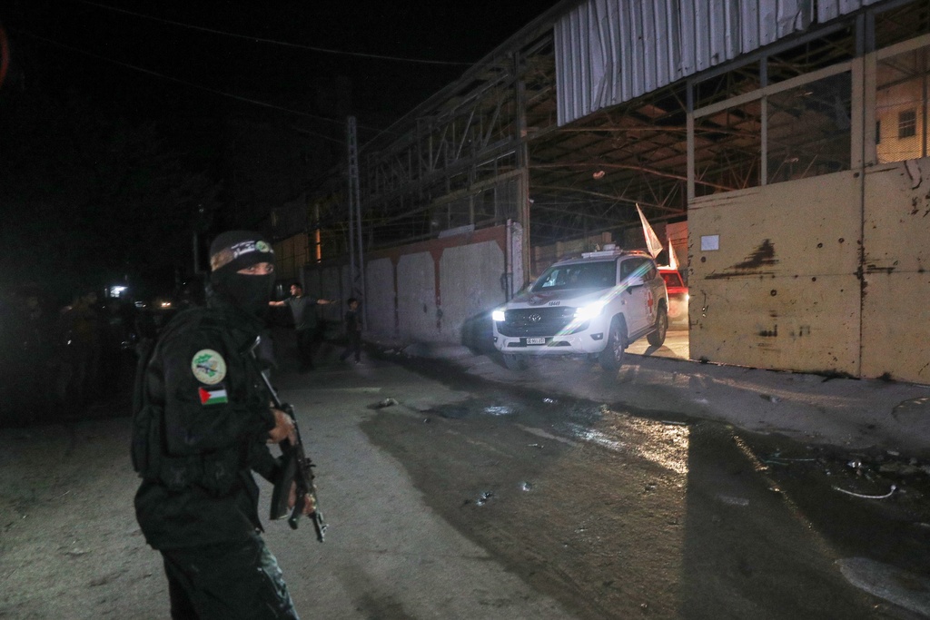 A gunman wearing the uniform of the al-Qassam Brigades, the military wing of Hamas, stands guard as Red Cross vehicles allegedly transporting coffins containing the bodies of four deceased hostages leave a warehouse for Israel, in Gaza City, Tuesday, Oct. 14, 2025. (AP Photo/Yousef Al Zanoun)