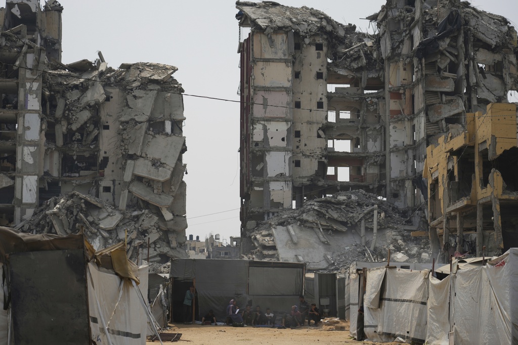 A group of Palestinians sit in the shade of their tent amid destroyed buildings on a hot summer day in Gaza City, Tuesday, Aug. 12, 2025. (AP Photo/Jehad Alshrafi)
