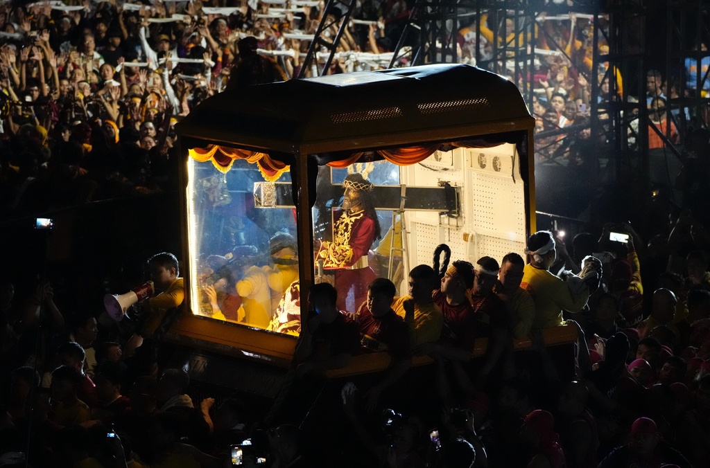 Catholic devotees walk beside a glass-covered carriage carrying the image of Jesus Nazareno during its annual procession in Manila, Philippines on its feast day on Friday Jan. 9, 2026. (AP Photo/Aaron Favila)
