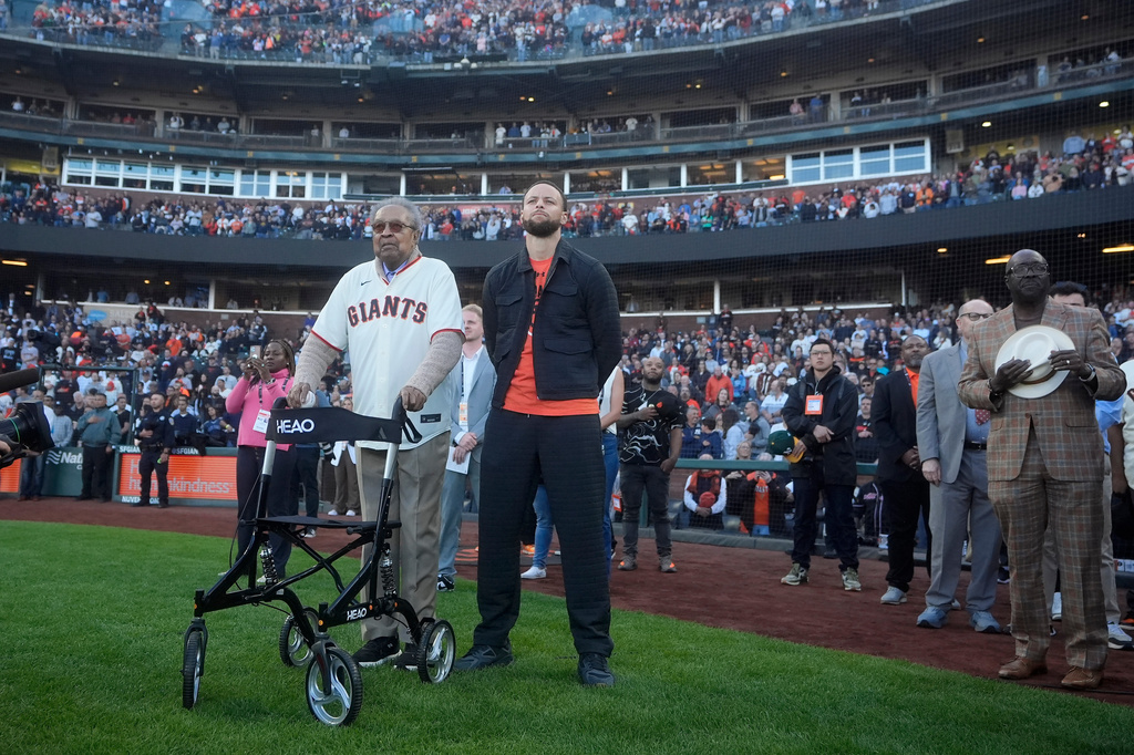 FILE - Dr. Clarence B. Jones, left, a former speech writer for Martin Luther King Jr., stands next to Golden State Warriors basketball player Stephen Curry, front right, during the playing of Lift Every Voice and Sing before a baseball game between the San Francisco Giants and the New York Yankees in San Francisco, May 31, 2024. (AP Photo/Jeff Chiu, File)