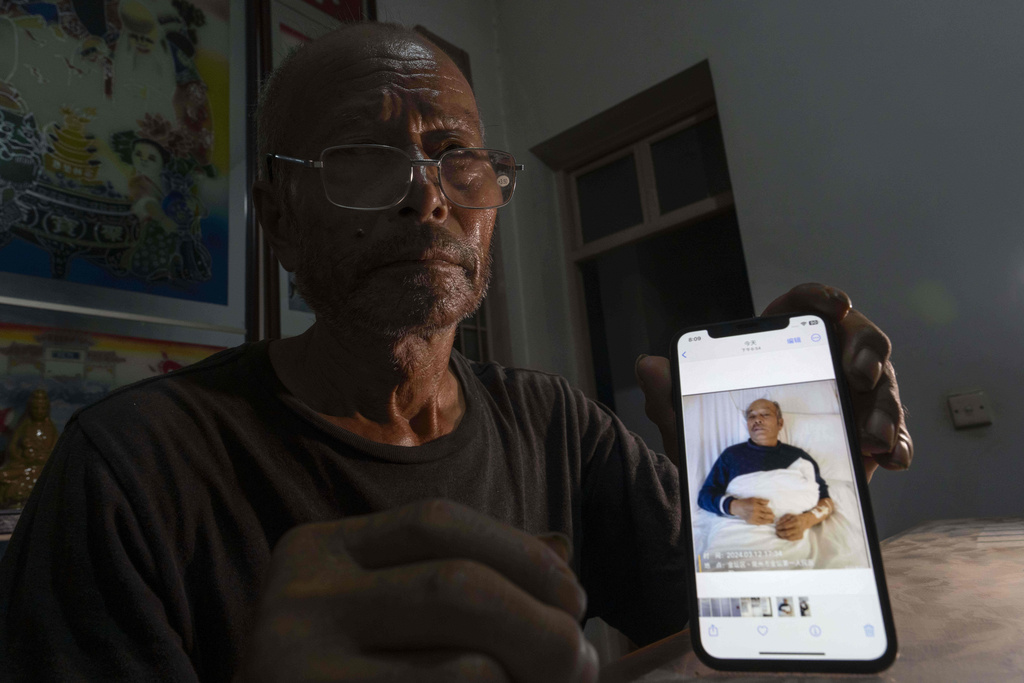 Yang Guoliang shows a March 12, 2024, photo of him lying in a hospital bed after police beat him with bricks, as he sits in his home in Changzhou in eastern China's Jiangsu Province, Sunday, Sept. 7, 2025. (AP Photo/Ng Han Guan)