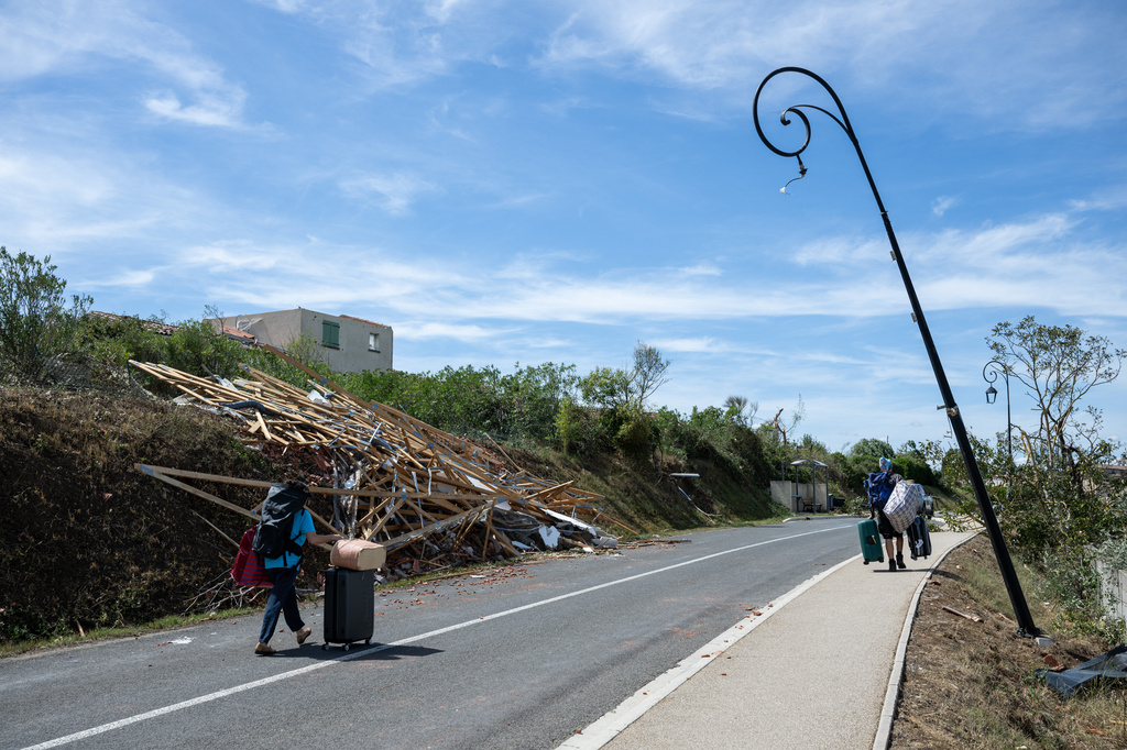 People leave with luggage after a tornado ravaged the small village of Pomas in southern France, leaving dozens injured, Tuesday Aug. 25, 2026. (AP Photo/Frederic Lancelot)
