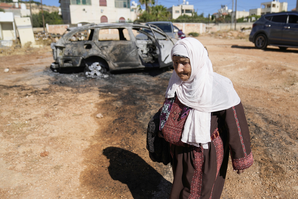 FILE - A woman walks past a vehicle that was burnt overnight by Israeli settlers in an attack that left three Palestinians killed and burnt several vehicles and damaged homes, according to residents in the West Bank village of Kafr Malik, east of Ramallah, Thursday, June 26, 2025. (AP Photo/Nasser Nasser, File)