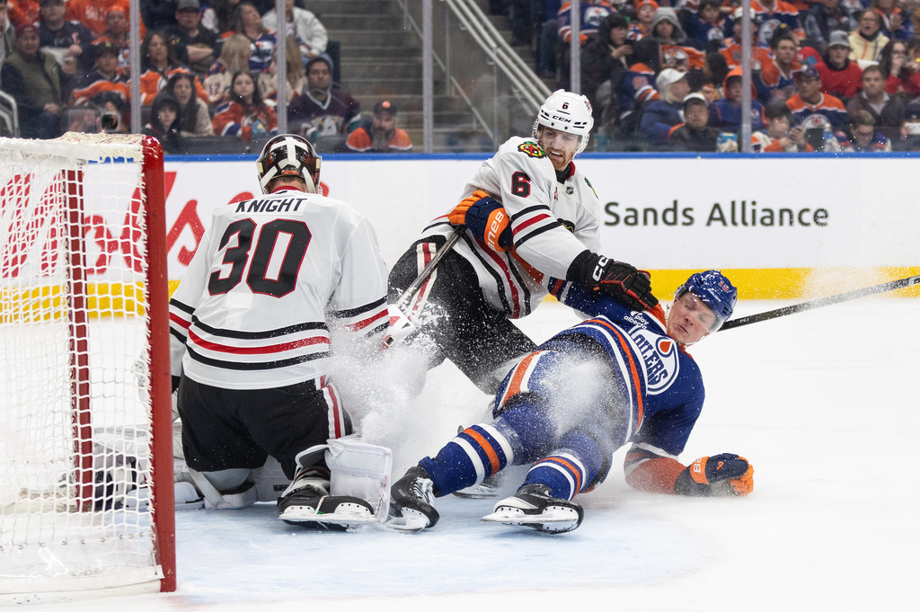 Chicago Blackhawks goalie Spencer Knight (30) makes the save as Sam Rinzel (6) and Edmonton Oilers' Trent Frederic (10) crash the net during the second period of an NHL game, in Edmonton on Thursday April 2, 2026. (Jason Franson/The Canadian Press via AP)
