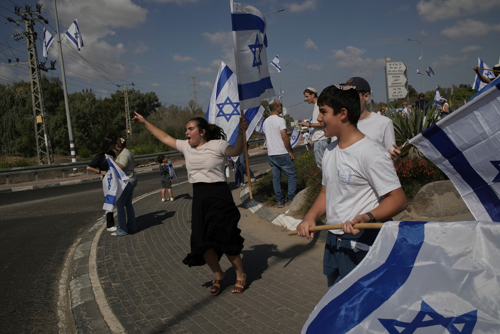 People wave Israeli flags on a street in southern Israel near the borders with Gaza as they celebrate the release of the hostages from the Gaza Strip, Monday, Oct. 13, 2025. (AP Photo/Leo Correa)