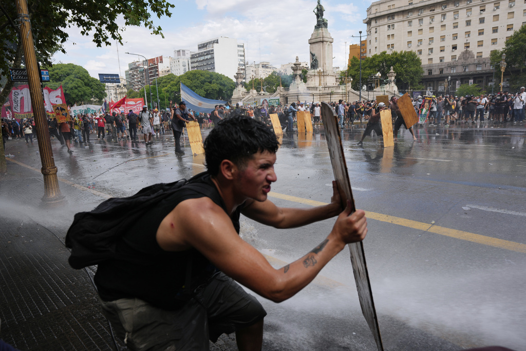 Protesters shield themselves with wooden boards as police spray water during clashes at a march by trade unions and opposition groups against a labor reform bill proposed by President Javier Milei's government in Buenos Aires, Argentina, Wednesday, Feb. 11, 2026. (AP Photo/Rodrigo Abd)