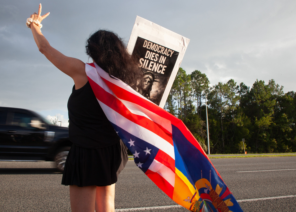 Patricia Ramos, of Palm Coast, wears a flag and waves at passing cars during a vigil for a Mexican man who was struck and killed by a tractor trailer while running from an encounter with Immigration and Customs Enforcements officers the day before, Wednesday, July 15, 2026, in St. Augustine, Fla. (AP Photo/Kelly Jordan)
