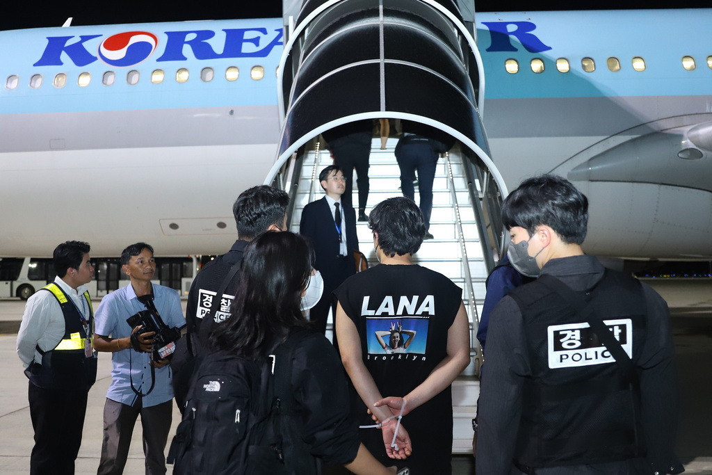 In this photo released by Agence Kampuchea Press (AKP), ons of South Koreans allegedly involved in online scams, center, is escorted by their police officers before boarding a plane at Techo International Airport in Kandal province, Cambodia, Friday, Oct. 17, 2025. (AKP via AP)