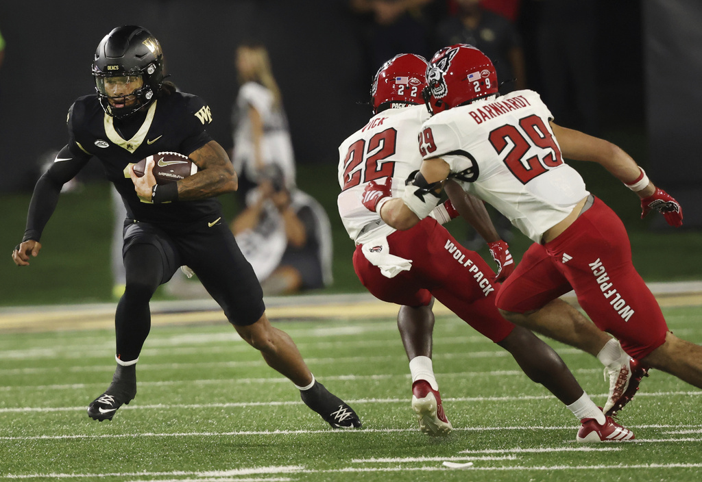 Wake Forest quarterback Robby Ashford, left, jukes past North Carolina State defensive backs Jackson Vick (22) and Brody Barnhardt (29) during an NCAA college football game Thursday, Sept. 11, 2025, in Winston-Salem, N.C. (Walt Unks/The Winston-Salem Journal via AP)