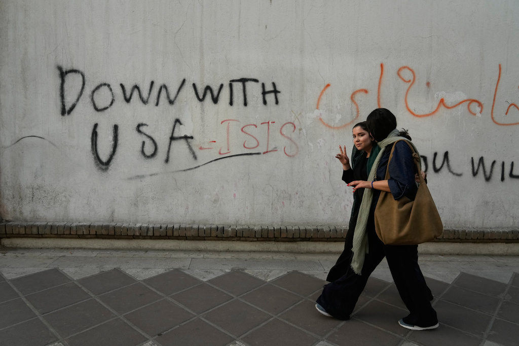 A woman reacts to the camera as she walks past an anti-U.S. graffiti painted on the wall of the British Embassy in Tehran, Iran, Saturday, June 6, 2026. (AP Photo/Vahid Salemi)