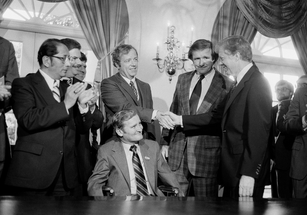FILE - President Jimmy Carter, right, shakes hands with the Michigan delegation, in Washington, April 24, 1980, who were present for the signing by Carter of a bill that would enable Volkswagen to operate an auto assembly plant in a Detroit suburb. Sen. Don Riegle, D-Mich., next to Carter, and Michigan Senate Majority Leader William Faust seated center, look on. (AP Photo, File)