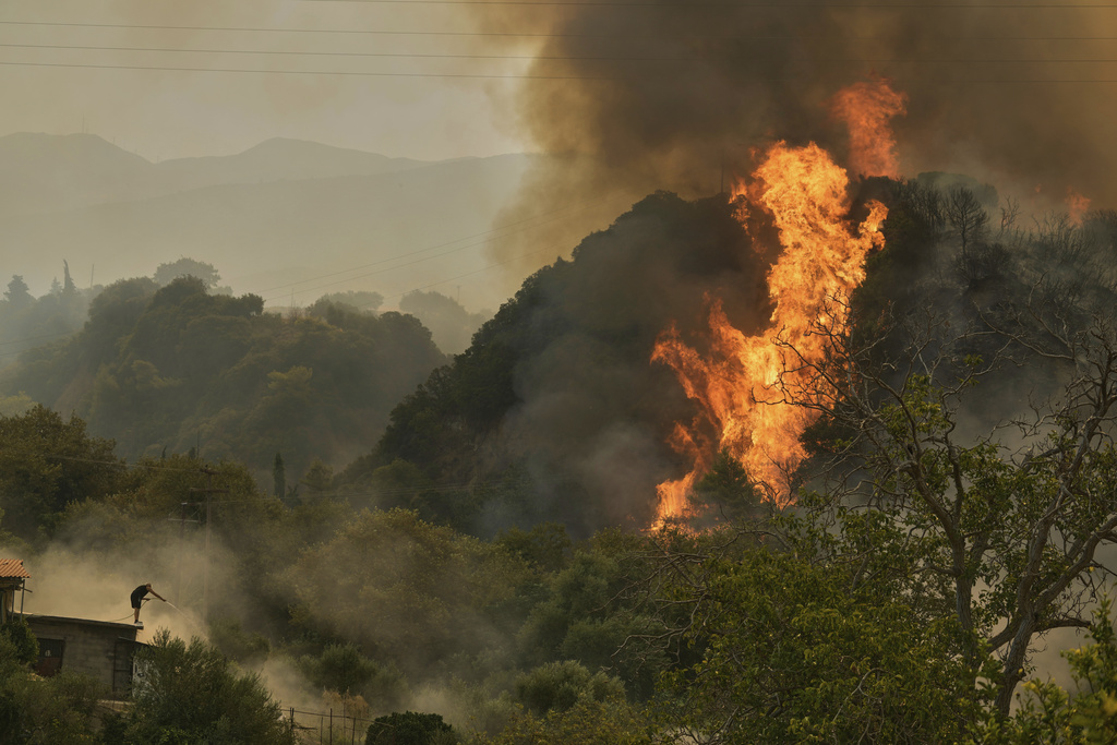 A man fights against the fire as approaching a house during a wildfire in Vounteni, on the outskirts of Patras, western Greece, Wednesday, Aug. 13, 2025. (AP Photo/Thanassis Stavrakis)