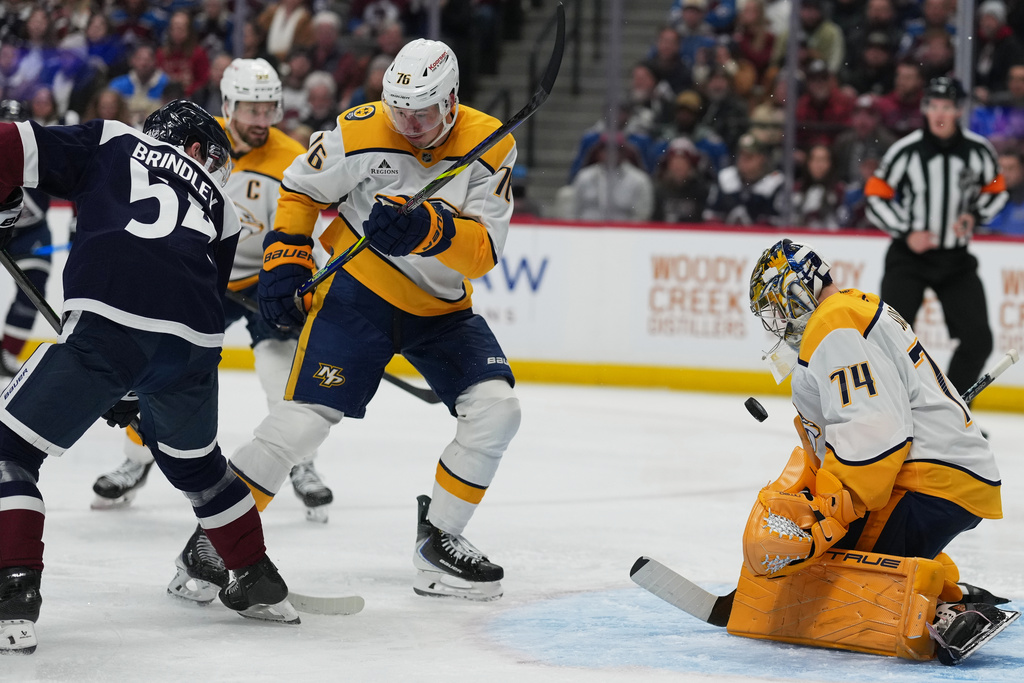 Colorado Avalanche center Gavin Brindley, left, redirects the puck past Nashville Predators defenseman Brady Skjei, center, as goaltender Juuse Saros stops the shot in the third period of an NHL hockey game Friday, Jan. 16, 2026, in Denver. (AP Photo/David Zalubowski)