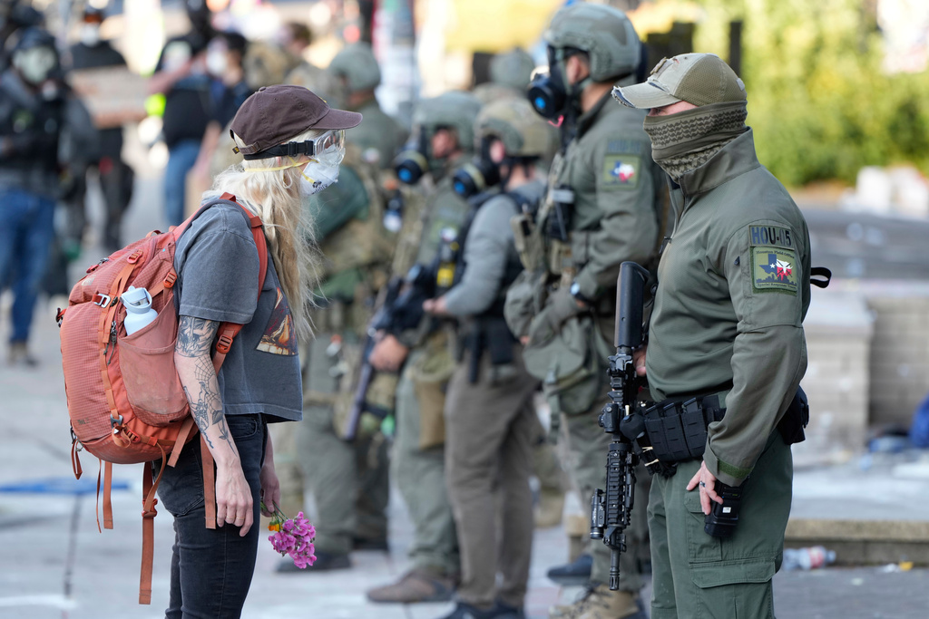 FILE - A woman stands off with a law enforcement officer wearing a Houston Field Office Special Response Team patch outside the U.S. Immigration and Customs building during a protest in Portland, Ore., June 14, 2025. (AP Photo/Jenny Kane, File)