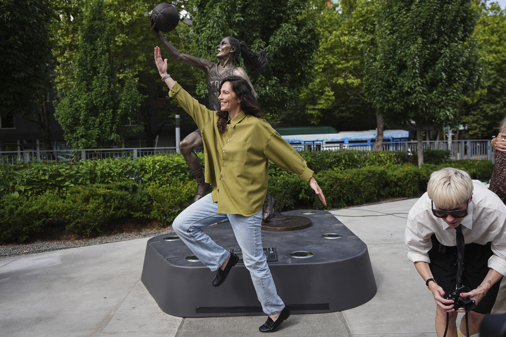 Former Seattle Storm WNBA basketball point guard Sue Bird poses for a photo with her statue after its unveiling as her partner, former United States and Seattle Reign soccer player Megan Rapinoe, right, runs to join photographers to take photos outside Climate Pledge Arena, Sunday, Aug. 17, 2025, in Seattle. (AP Photo/Lindsey Wasson)