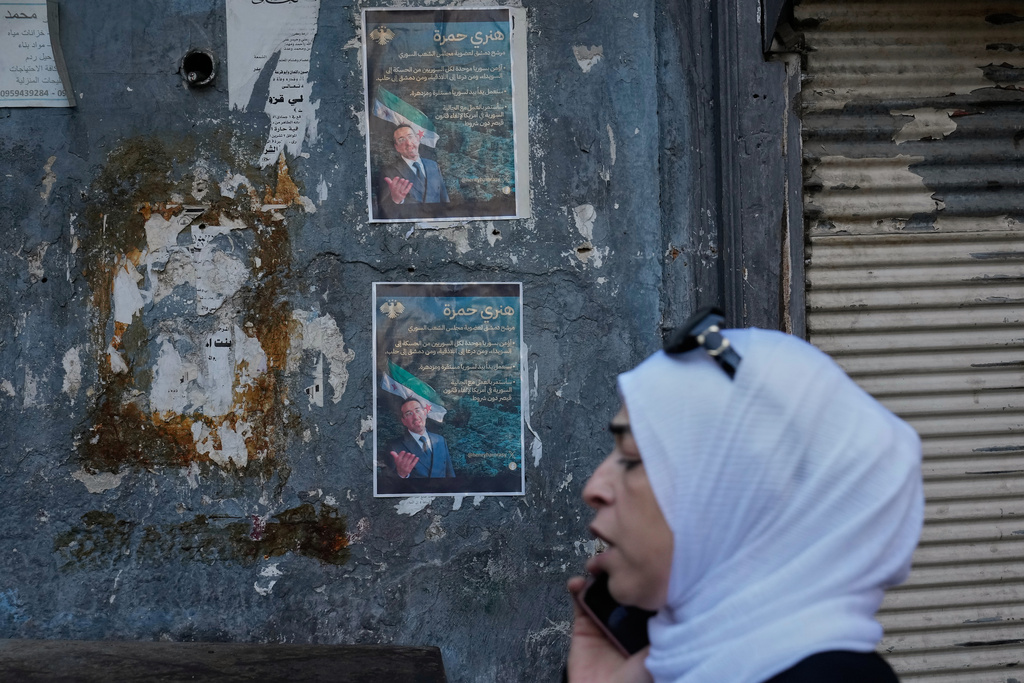 A Syrian woman passes in front of posters showing Syrian-American Jew Henry Hamra, a candidate for the Syrian Parliamentary elections, in the Jewish neighborhood of old Damascus, Syria Friday, Oct. 3, 2025. (AP Photo/Hussein Malla)