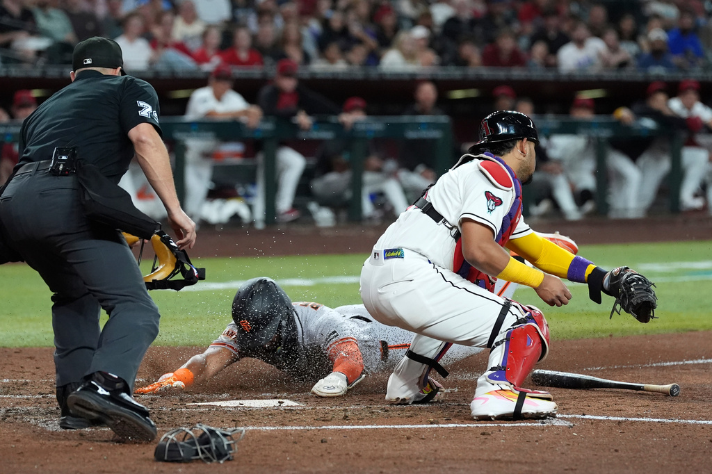 San Francisco Giants' Victor Bericoto, center, scores a run as Arizona Diamondbacks catcher Gabriel Moreno reaches to apply a late tag as umpire Tripp Gibson, left, looks on during the fifth inning of a baseball game, Monday, June 29, 2026, in Phoenix. (AP Photo/Ross D. Franklin)