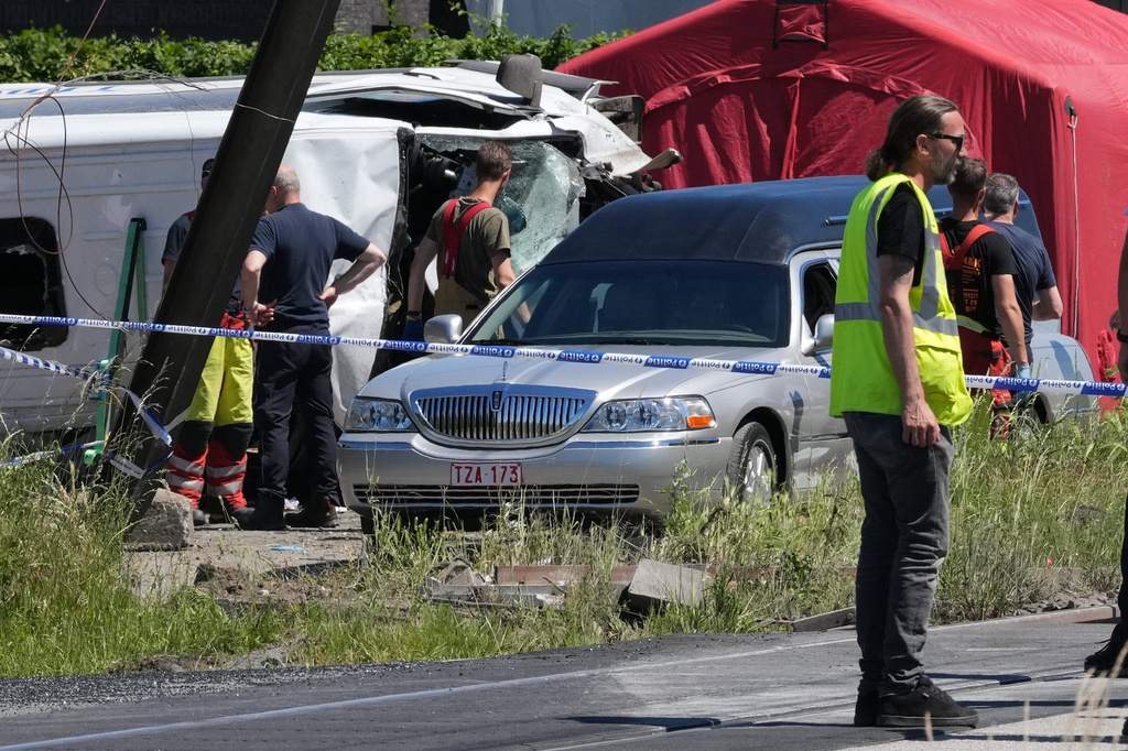 A hearse drives away at a level crossing where a train collided with a school van in Buggenhout, Belgium, Tuesday, May 26, 2026. (AP Photo/Marius Burgelman)