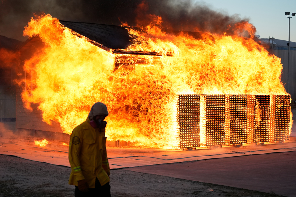 A wildfire researcher walks in front of an accessory dwelling unit burning during an experiment at the Institute for Business & Home Safety center on Thursday, April 16, 2026, in Richburg, S.C. (AP Photo/Erik Verduzco)